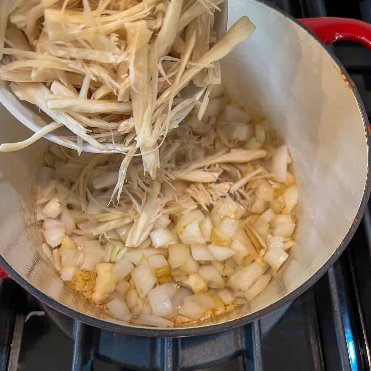 Shredded oyster mushrooms being added to the pot with sautéed onion. 