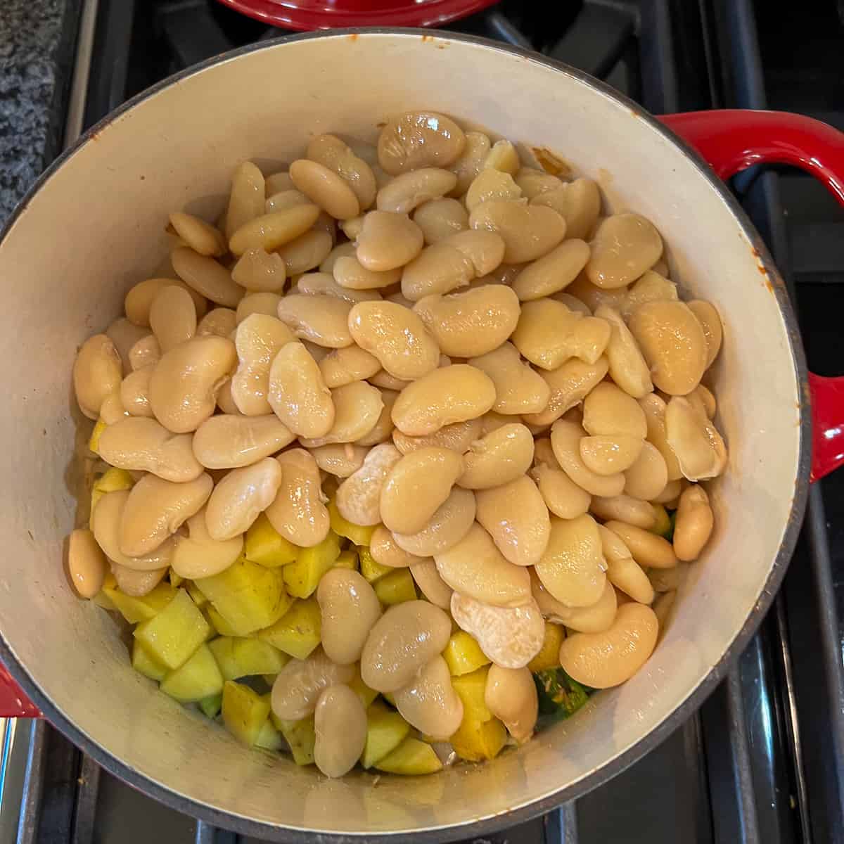 A pot with large lima beans and diced potatoes on top of other veggies.