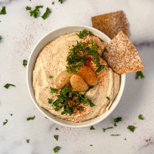 Butter bean hummus in a bowl topped with fresh chopped parsley and a dusting of smoked paprika.