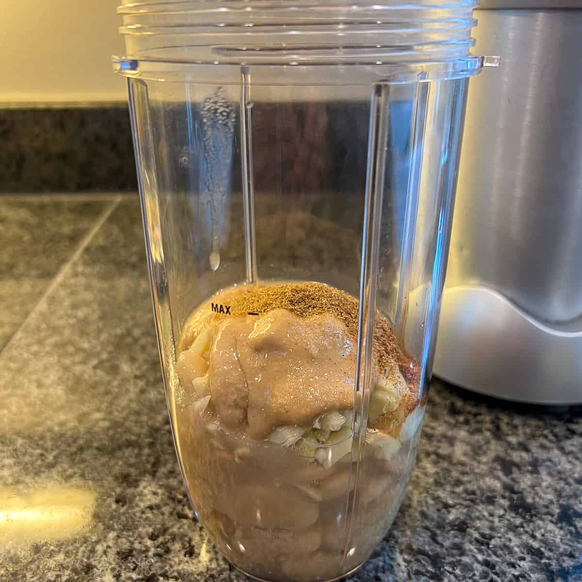 Butter beans, tahini, liquid, and spices in a blender cup before blending. 