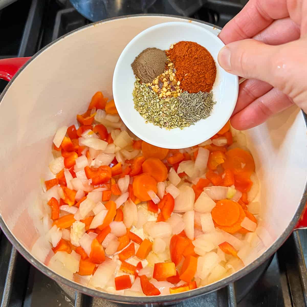 Dried spices being added to a pot with vegetables on the stovetop.