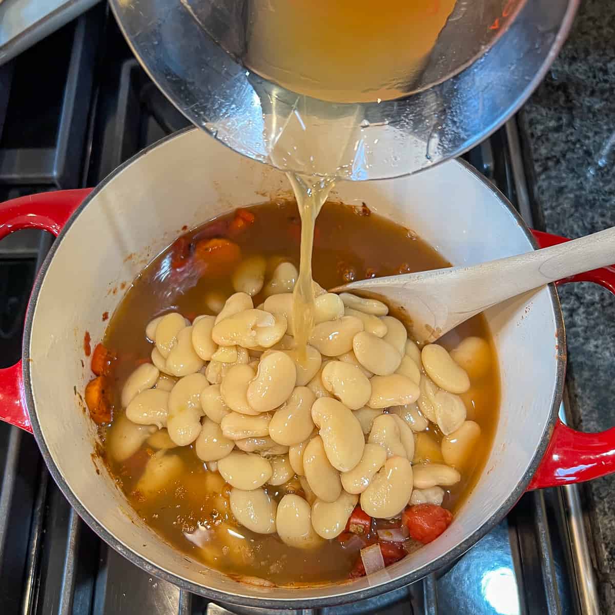 Low sodium vegetable broth being added to the pot with butter beans and vegetables.