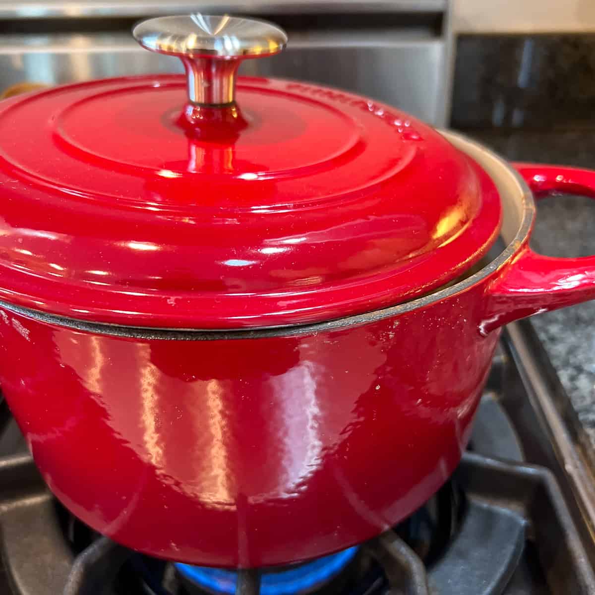 A side view of the soup pot with lid partially covering the pot and flame on the stovetop.