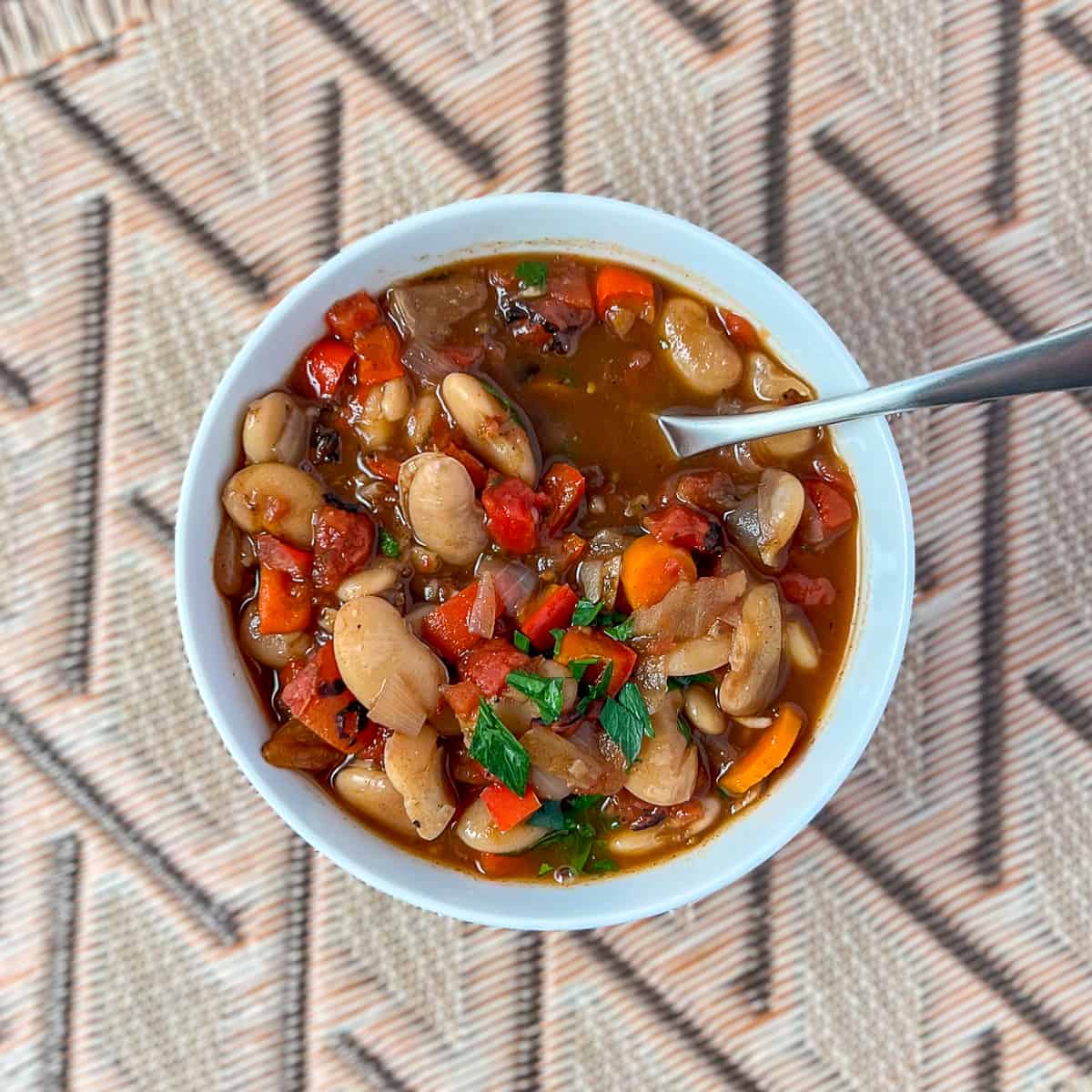 A bowl of butter bean stew topped with fresh chopped parsley and spoon on the side.