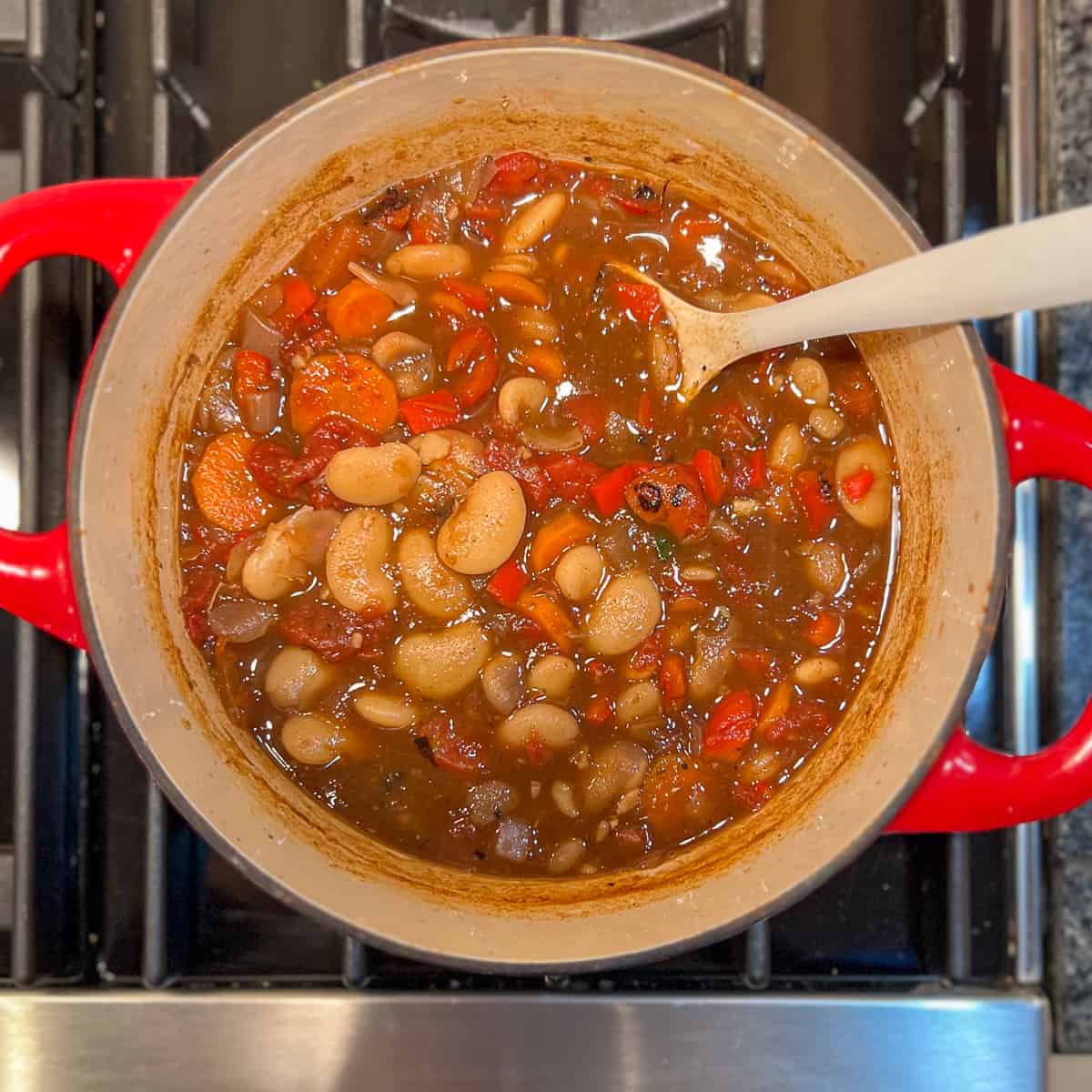 Butter bean stew in a pot on the stovetop with wooden spoon.