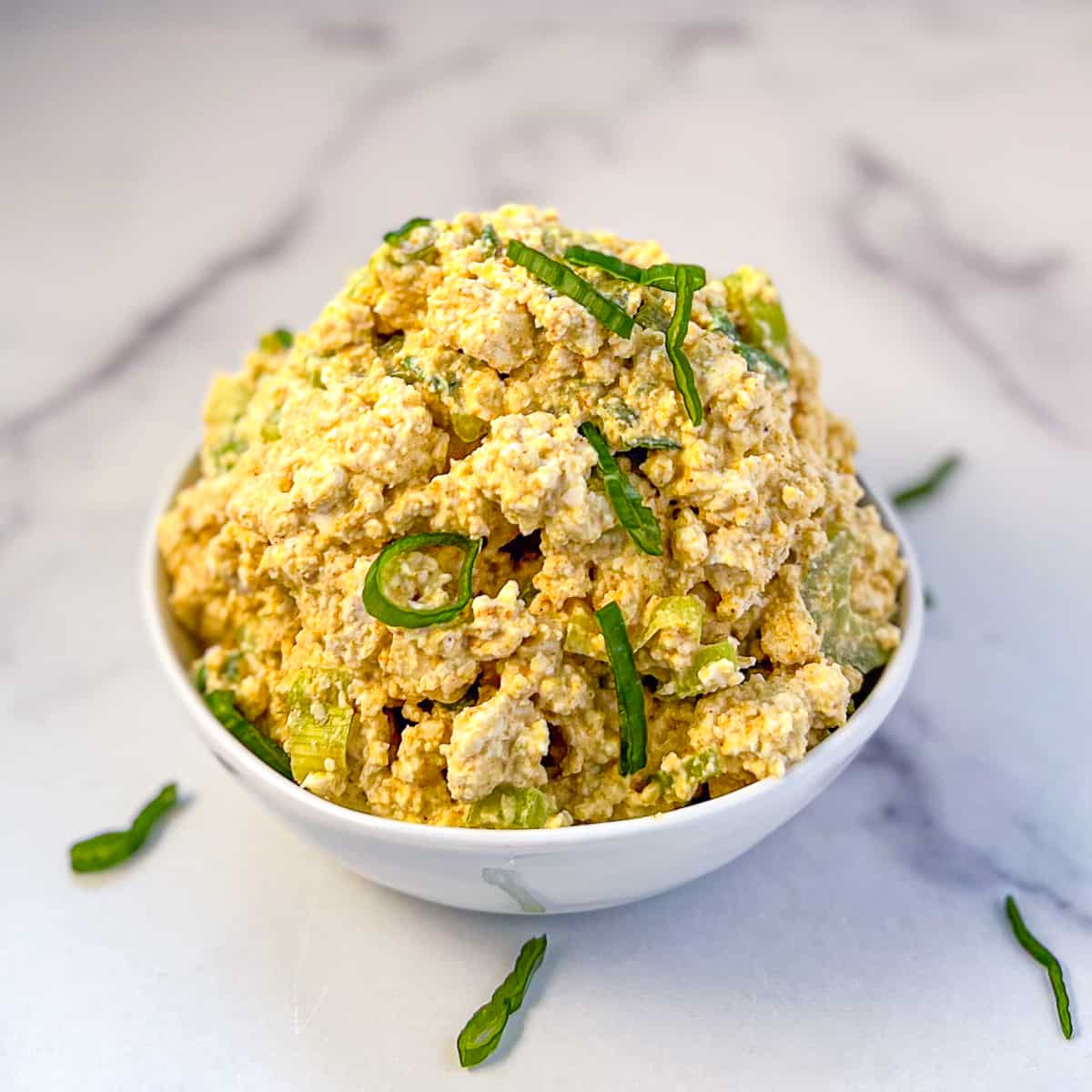 Curry tofu salad in a bowl with thinly sliced green onion.