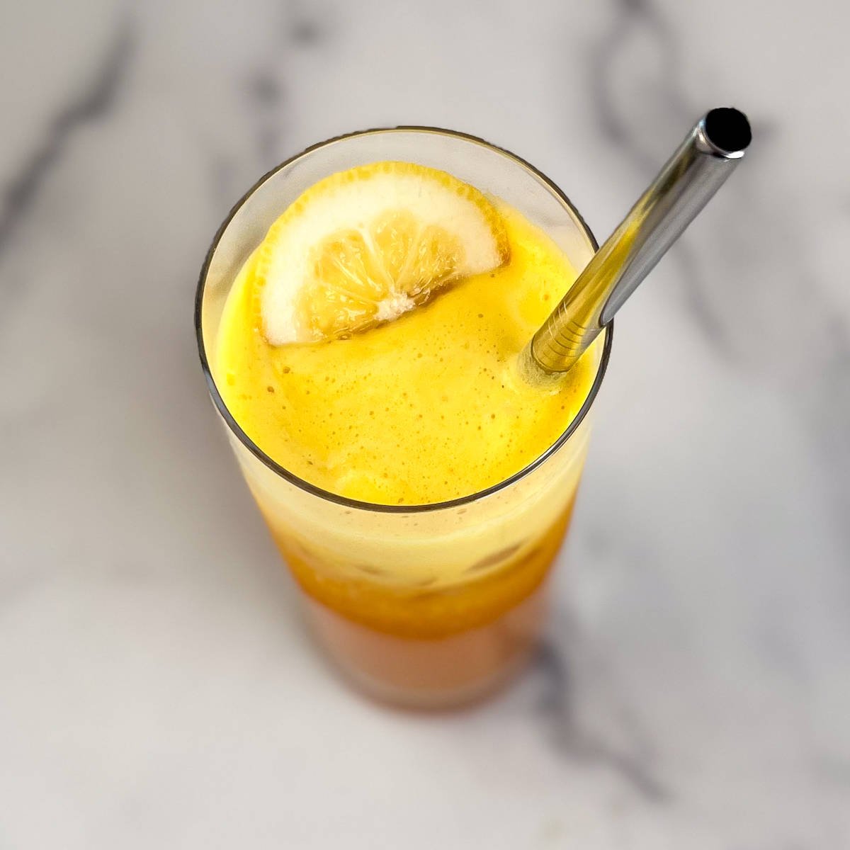 Glass of golden beet juice with slice of lemon on top and metal straw.