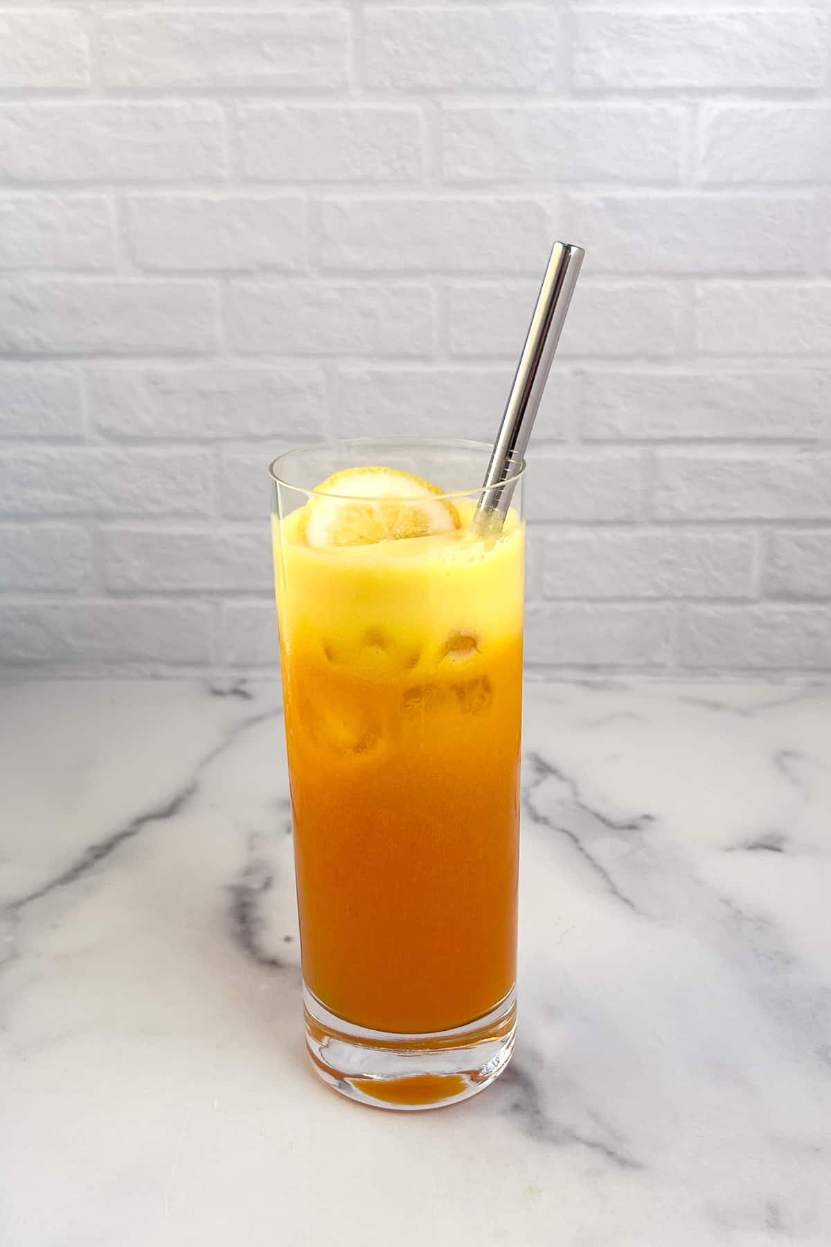 Tall glass of golden beet juice with fresh lemon and a metal straw.