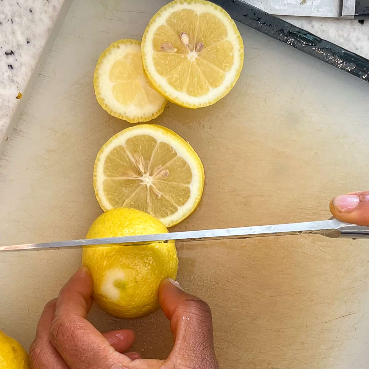 A woman's hand slicing lemons for the juicer.