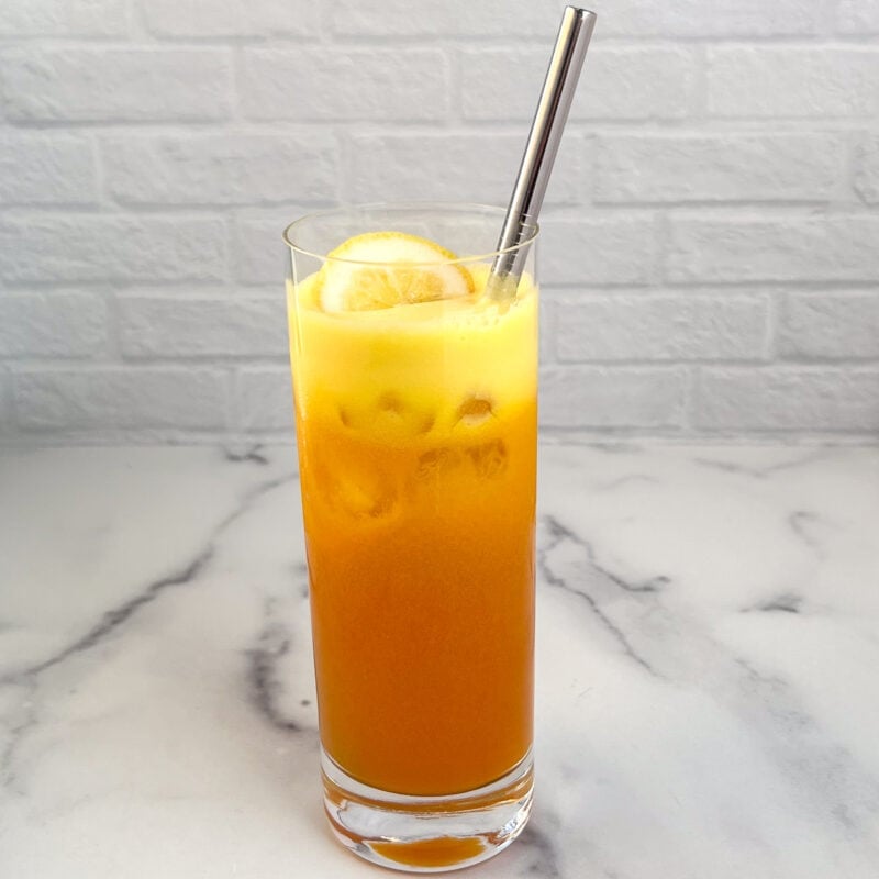 Glass of golden beet juice with a metal straw.