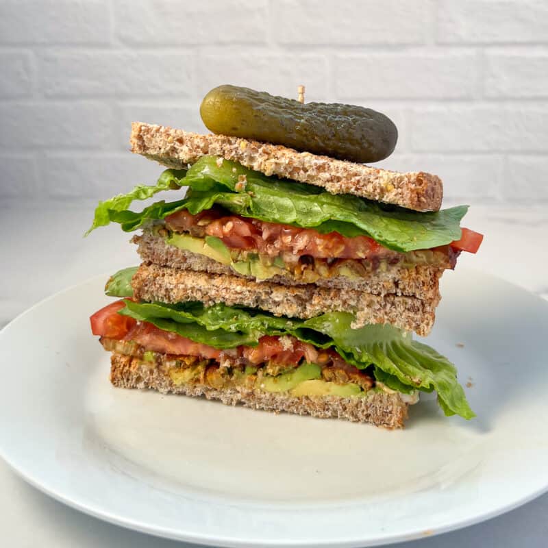 Tempeh BLT stacked on each other with dill pickle on top.