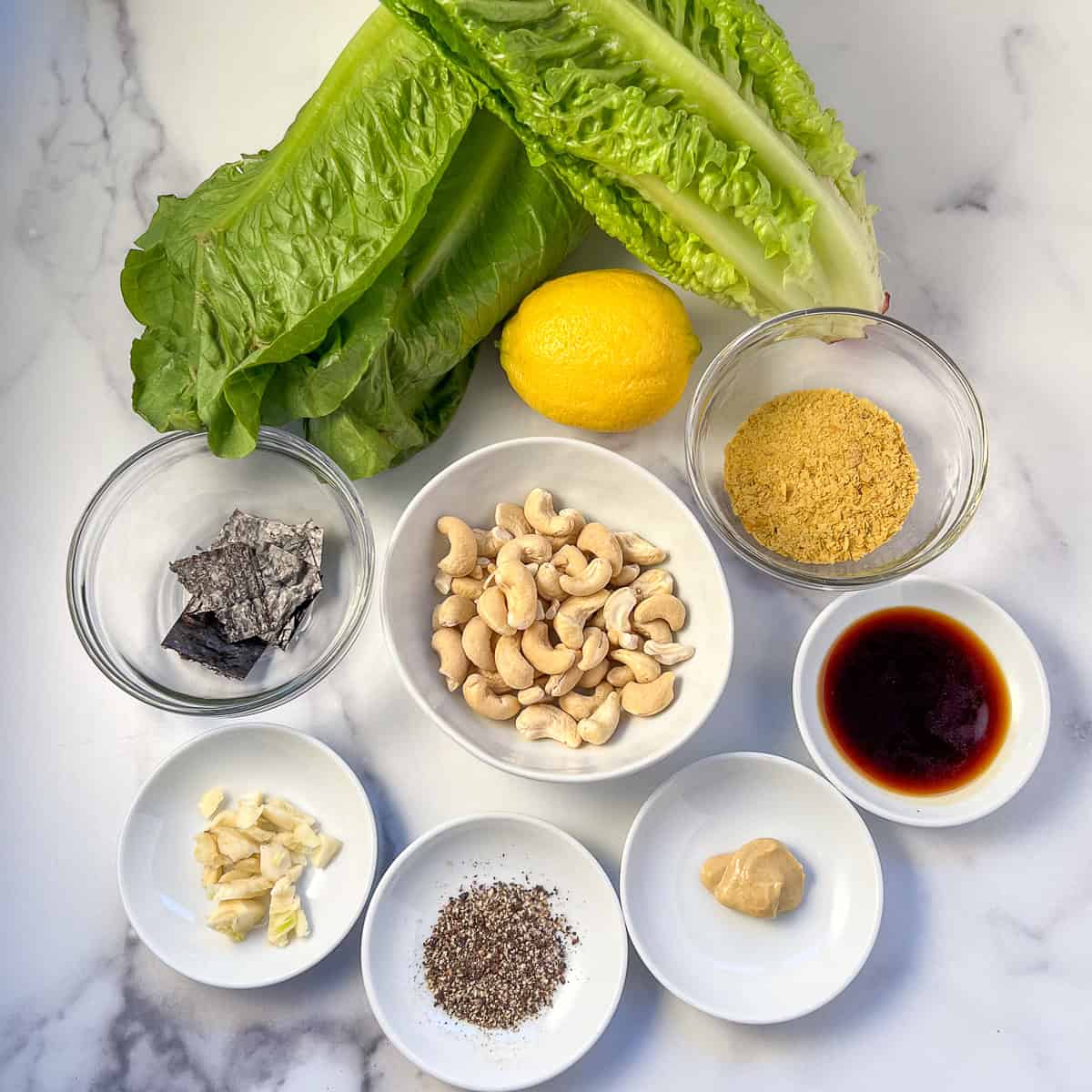 Ingredients for vegan caesar salad: romaine lettuce, lemon, cashews, nori, nutritional yeast, garlic, dijon mustard and black pepper.