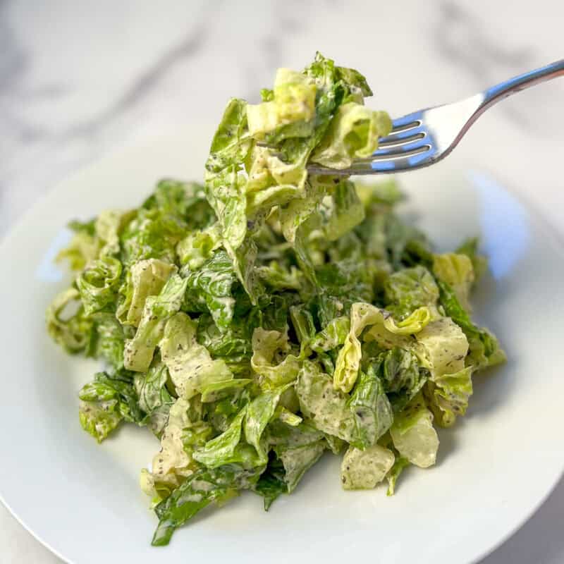 Vegan caesar salad on a plate with a fork dishing up a bite.
