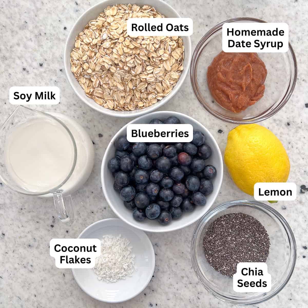 Ingredients for Lemon Blueberry Overnight Oats: rolled oats, blueberries, simple homemade date syrup, lemon, chia seeds, soymilk and unsweetened coconut flakes.