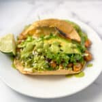 Two green goddess tacos on a plate with fresh lime wedge.