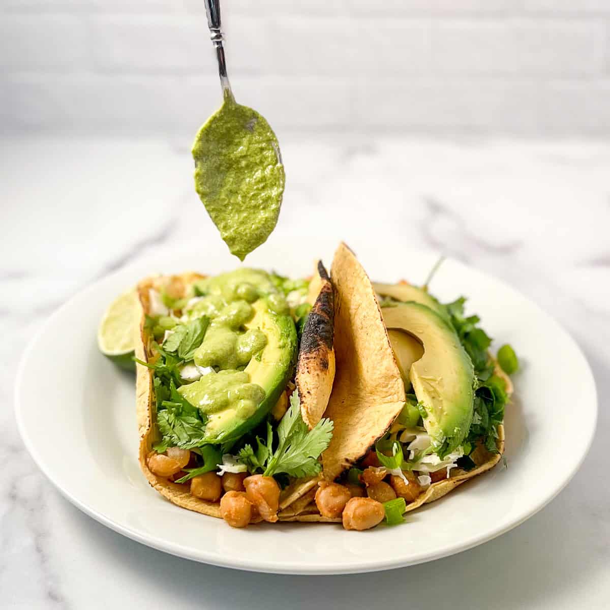 A spoon drizzling green goddess dressing onto green goddess tacos.