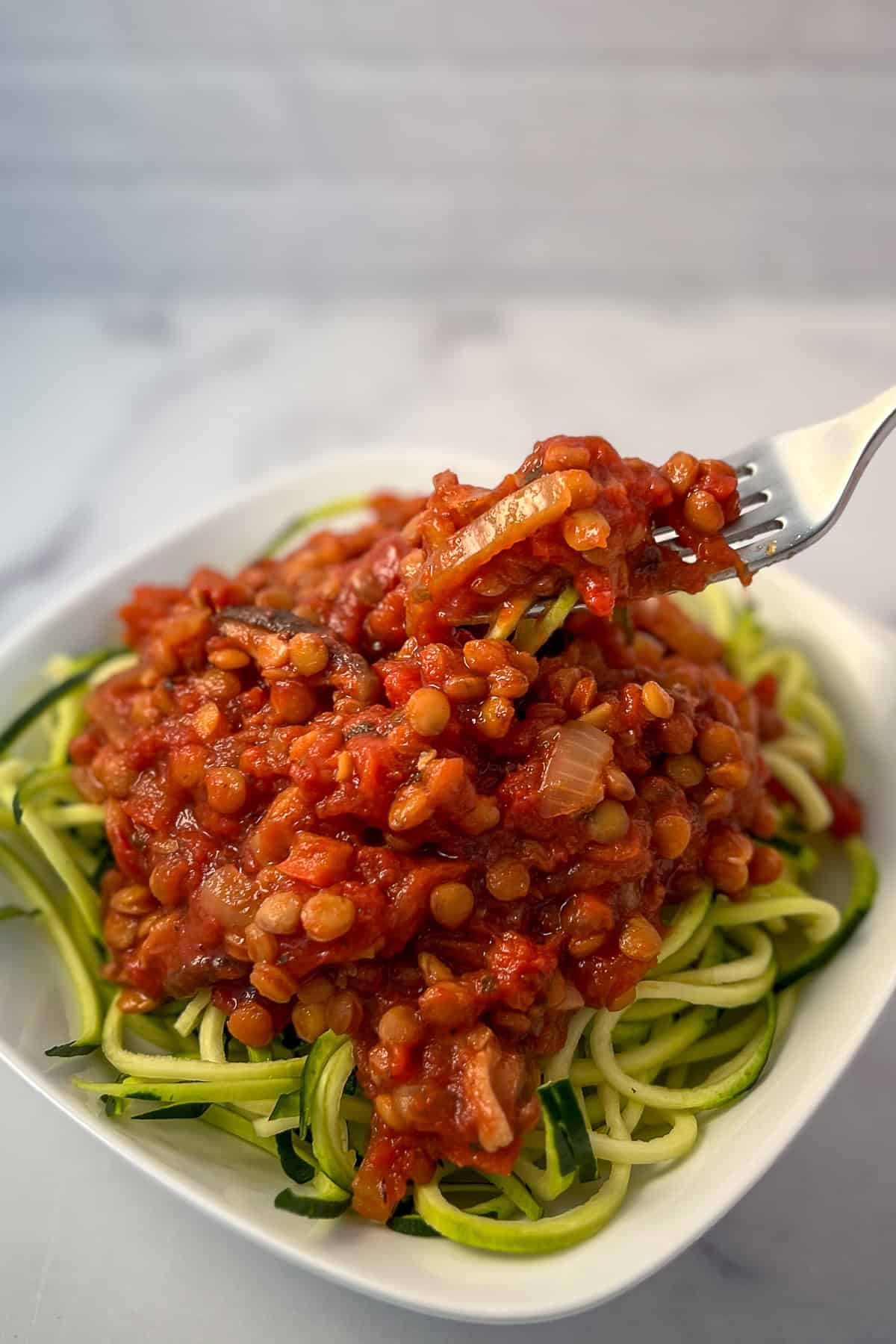 Green lentil bolognese over raw zucchini spiralized pasta in a bowl with fork.