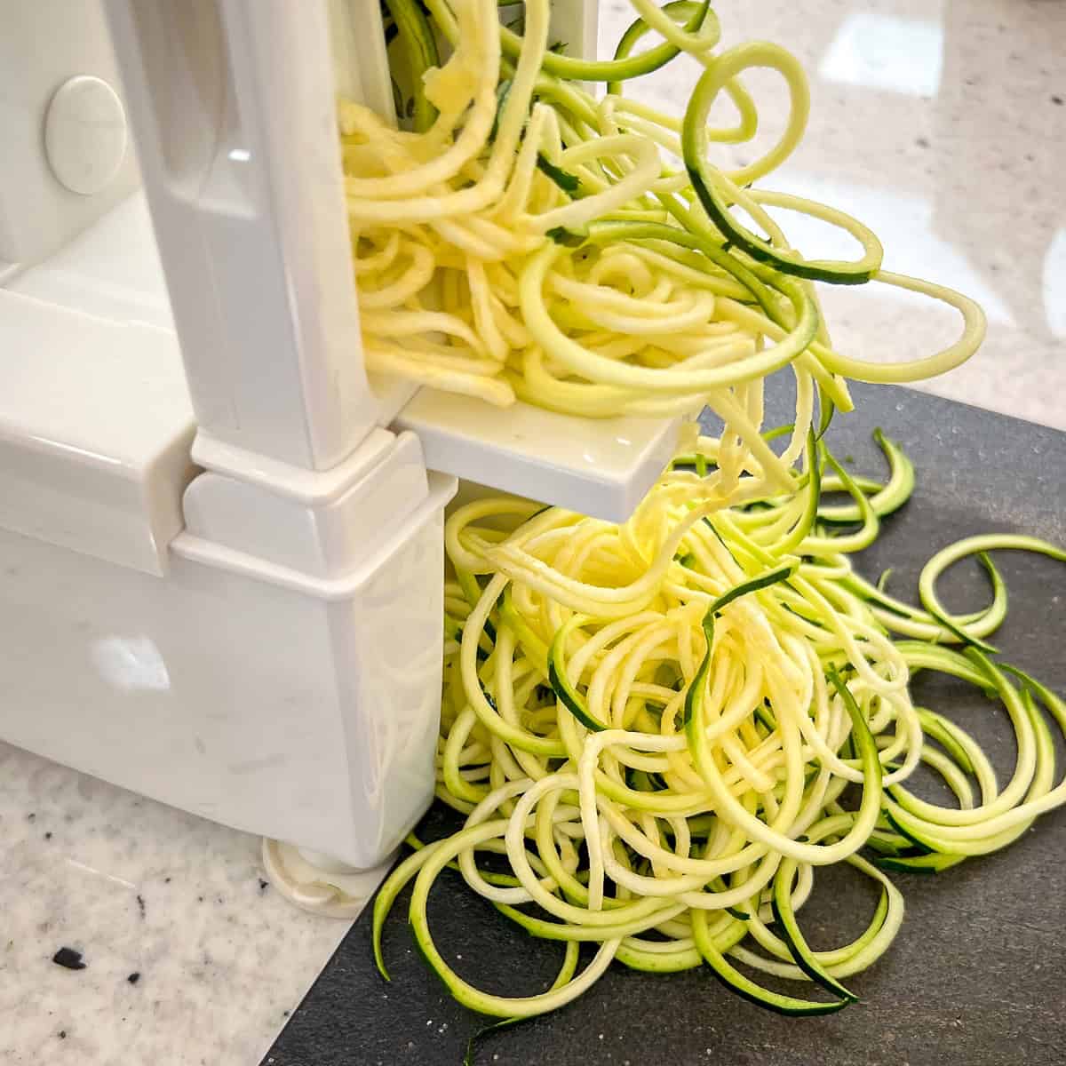 Zucchini pasta being made in a spiralizer on a cutting board.