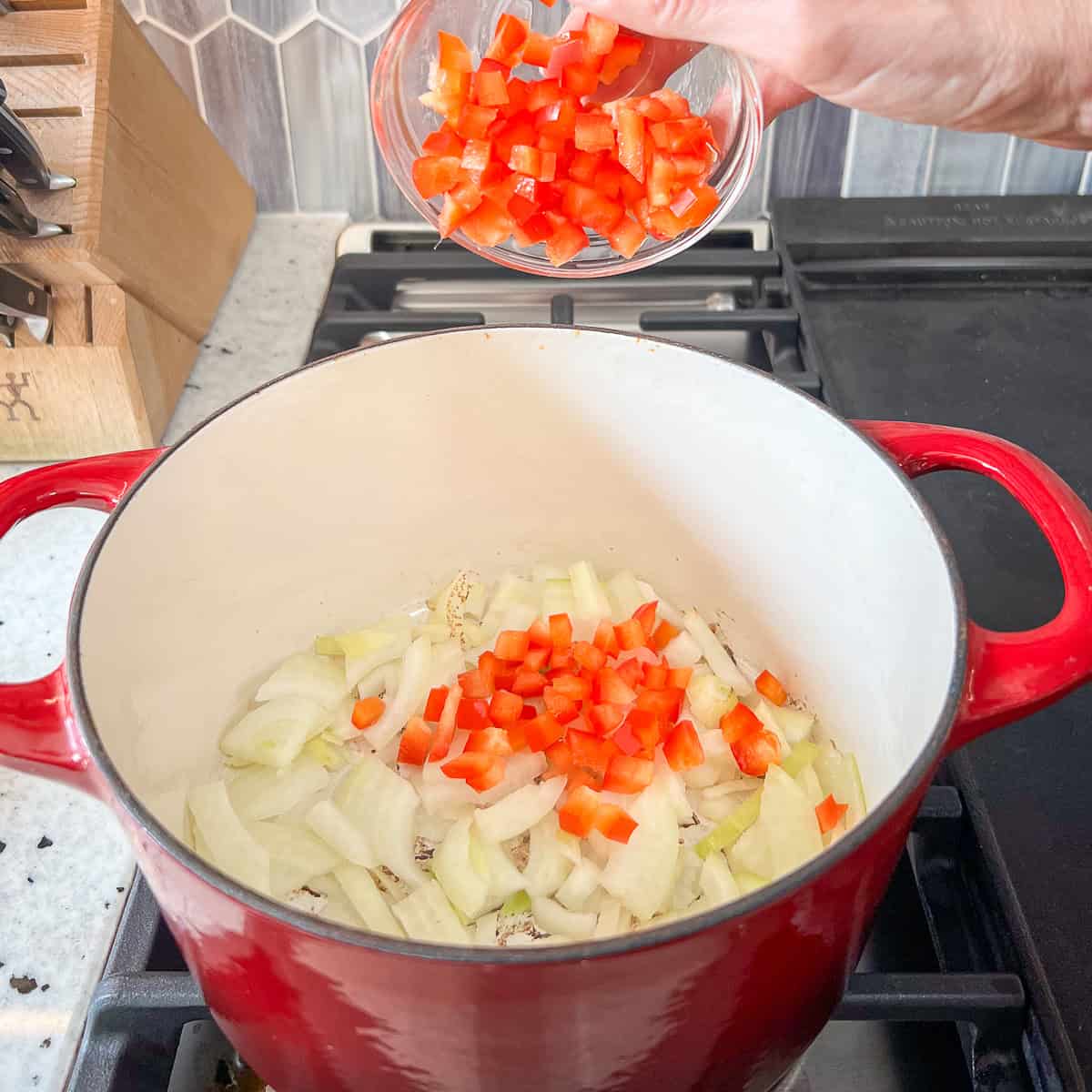 Diced red bell pepper being added to the pot with onions.