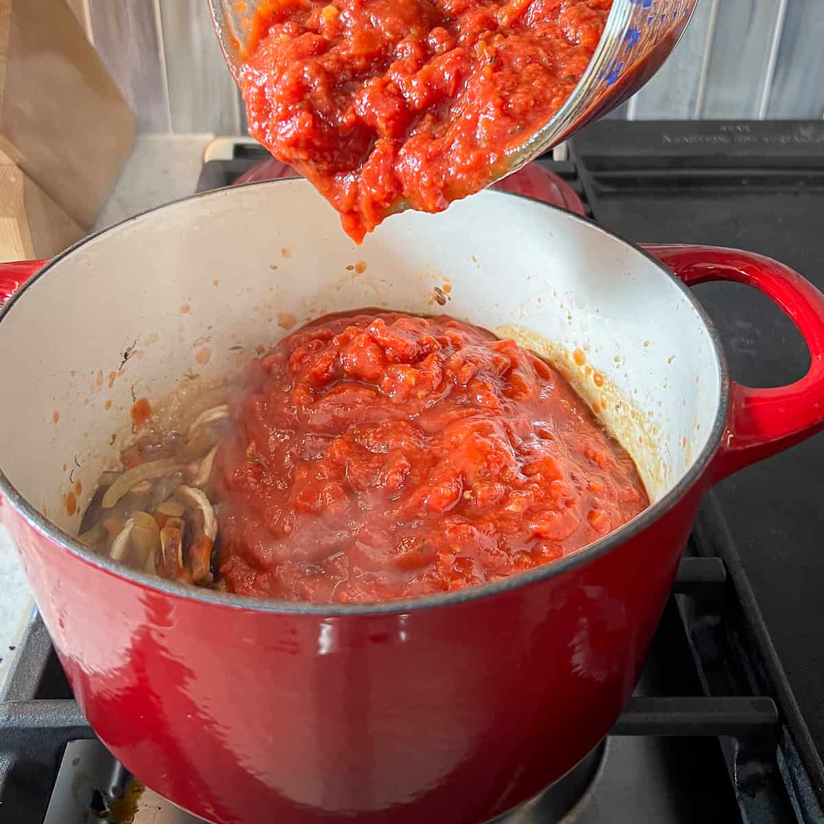 Spaghetti sauce being added to the pot with mushrooms.