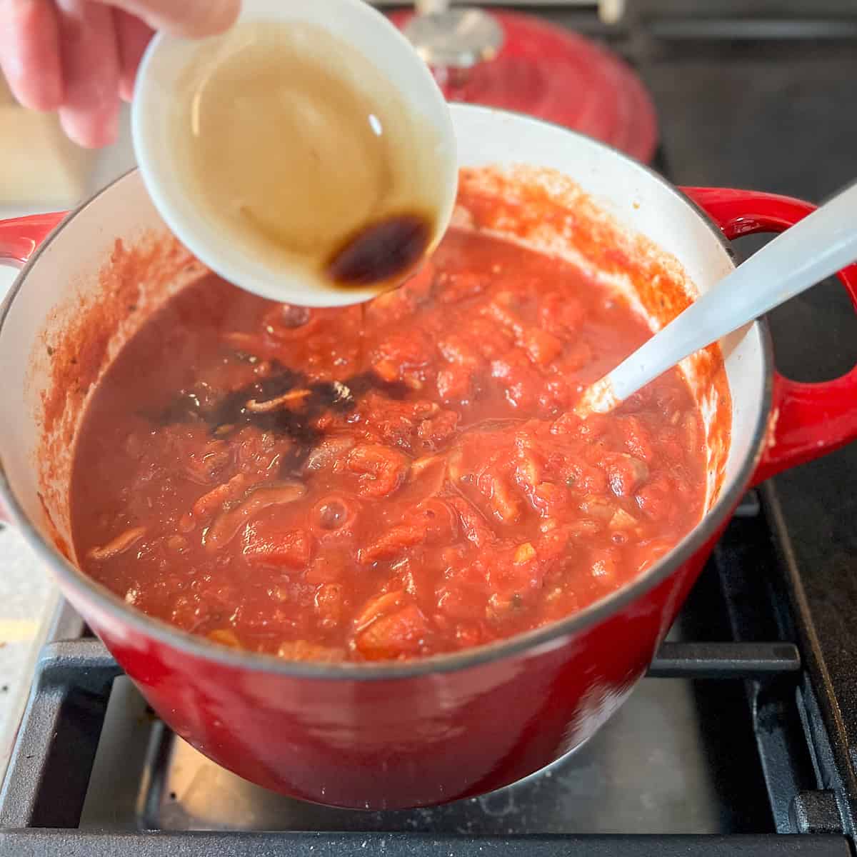 Balsamic vinegar being poured into a pot of tomato sauce.