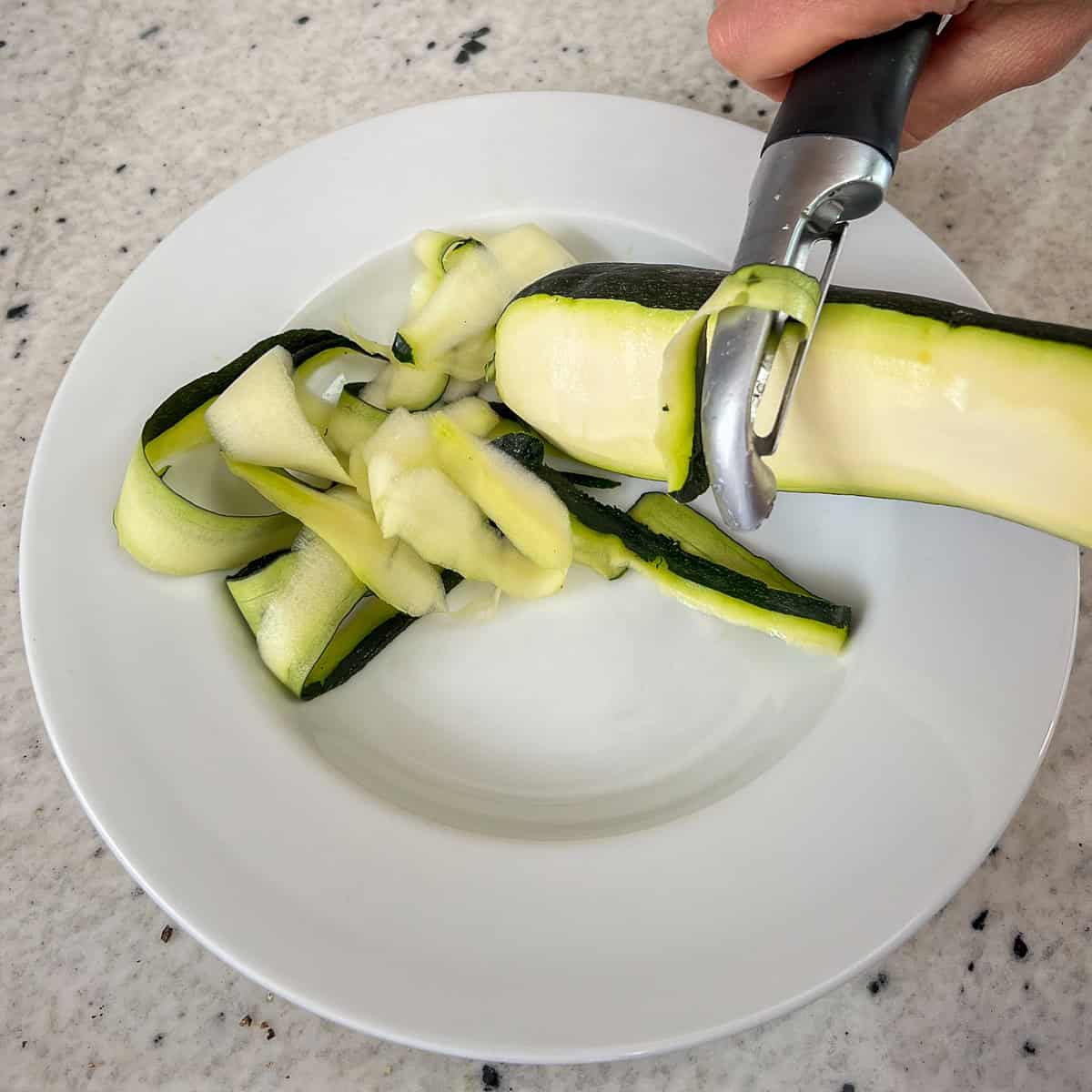 Using a peeler to make zucchini pasta ribbons.