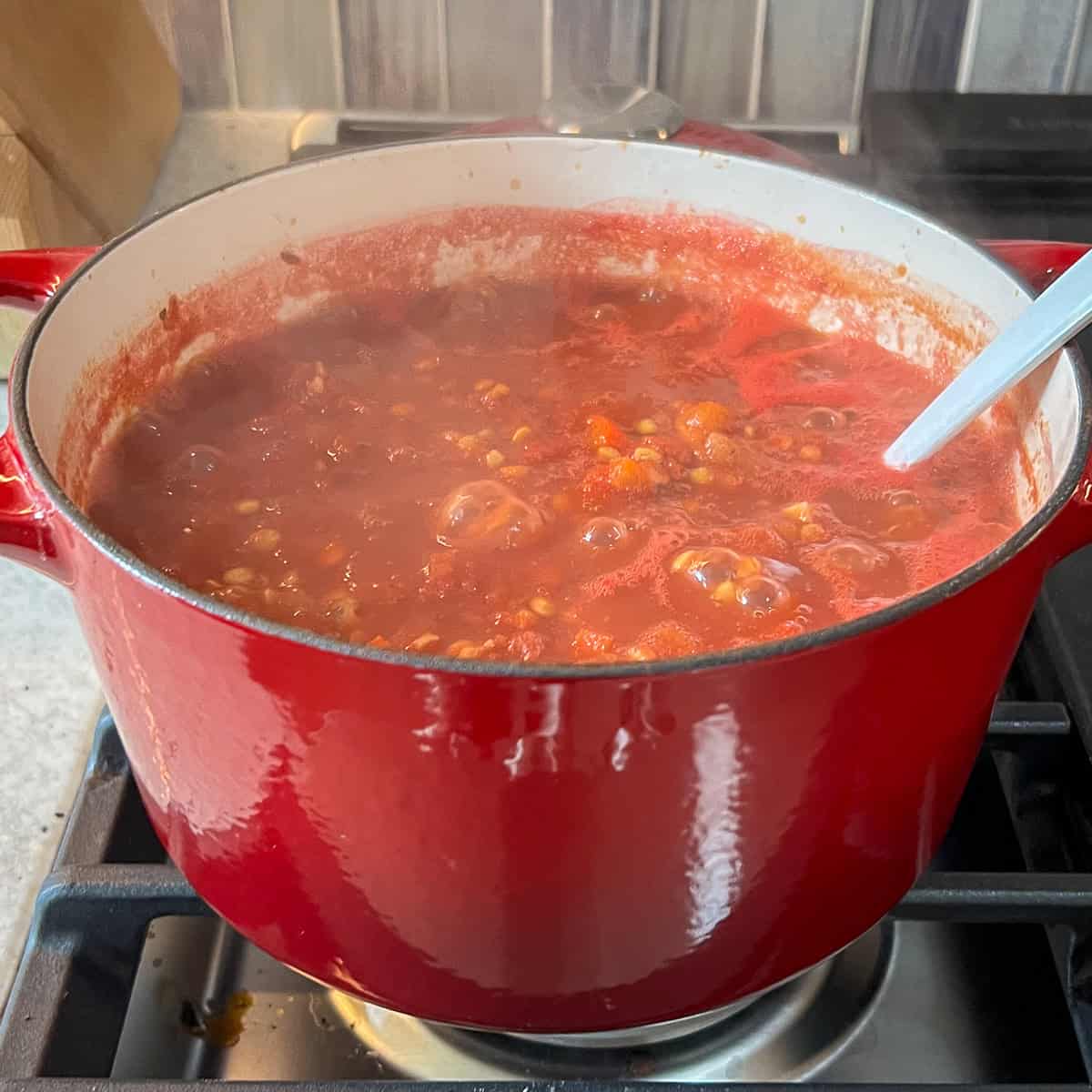 A bubbling pot of lentil bolognese on the stovetop with cooking spoon.