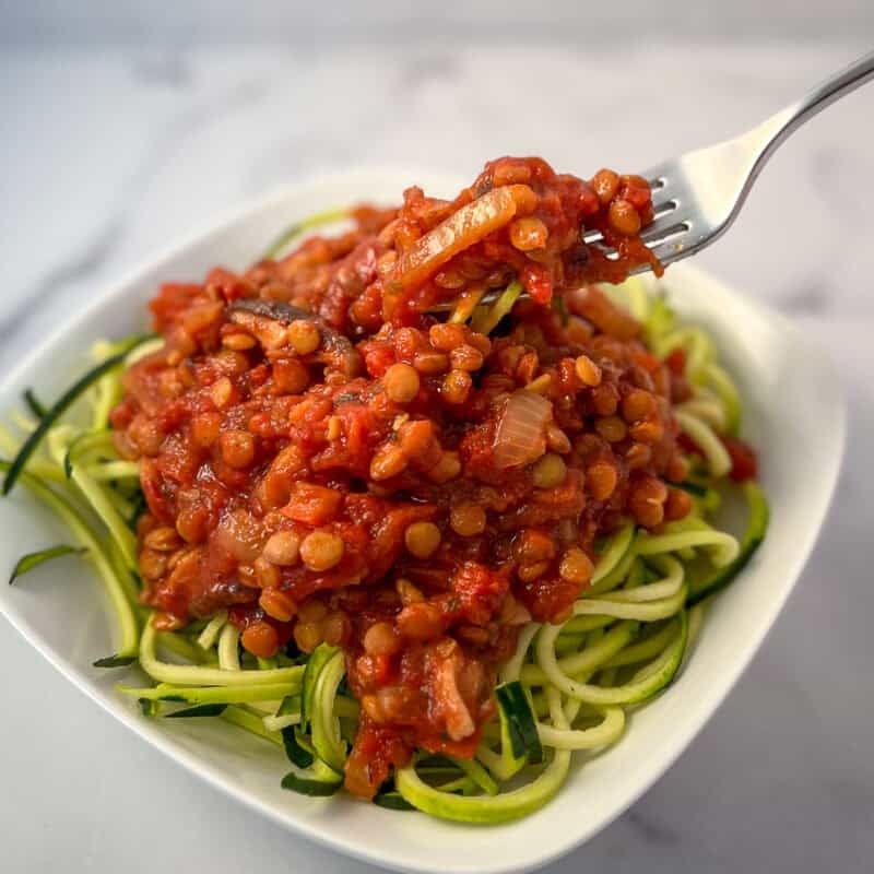 Vegan lentil bolognese over zucchini pasta in a bowl with a fork.