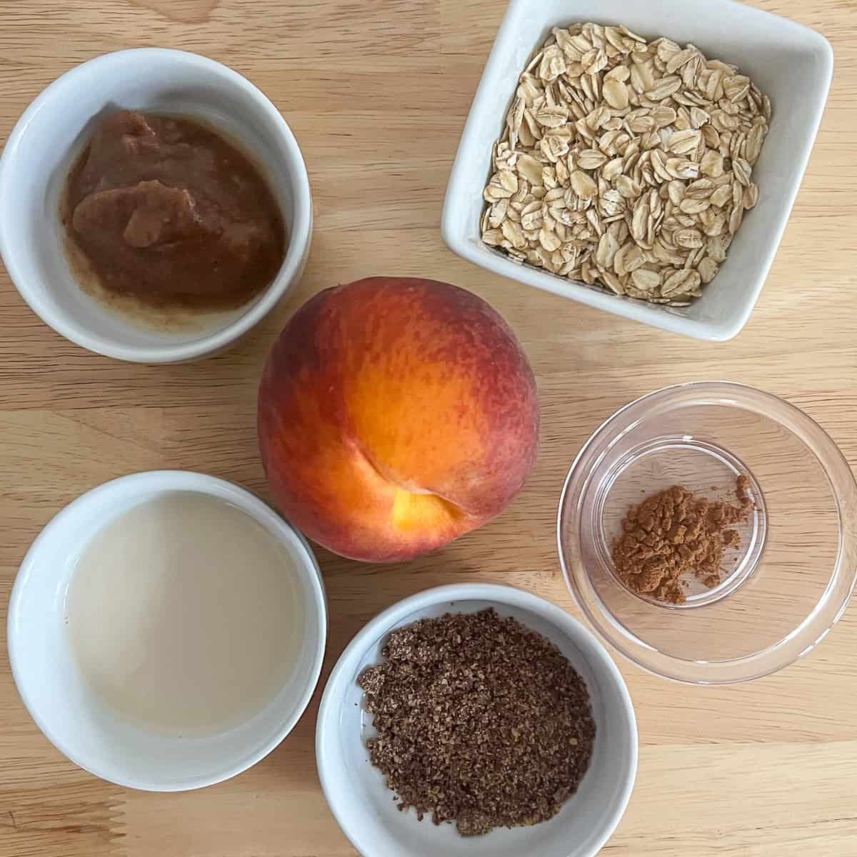 Ingredients for healthy peach cobbler: rolled oats, date syrup, fresh peach, cinnamon, ground flaxseeds, plant based milk.