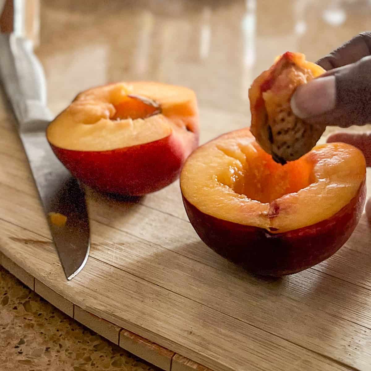 A peach cut in half with pit being pulled out.