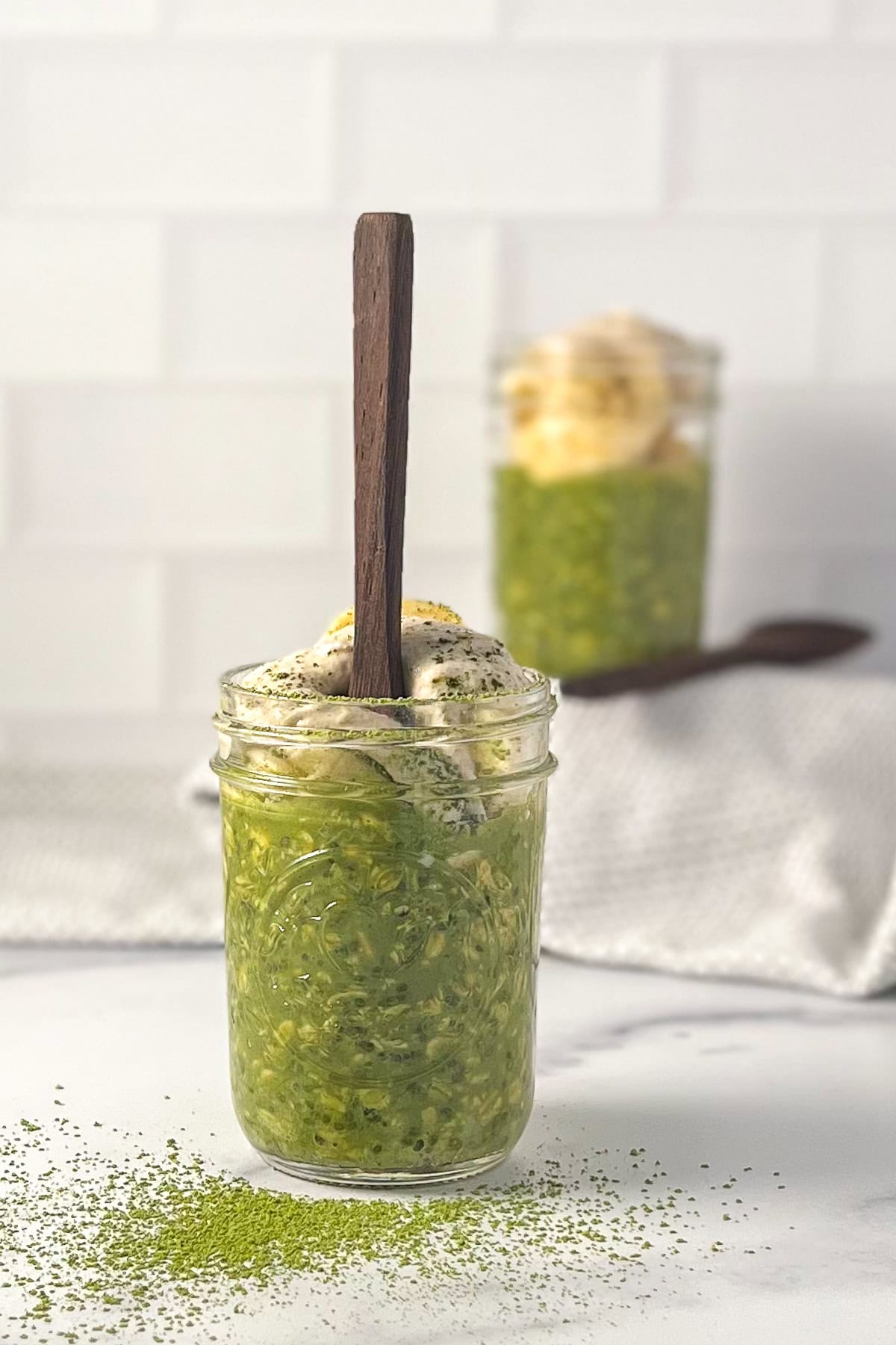 Matcha overnight oats in a mason jar with a wooden spoon sticking out.