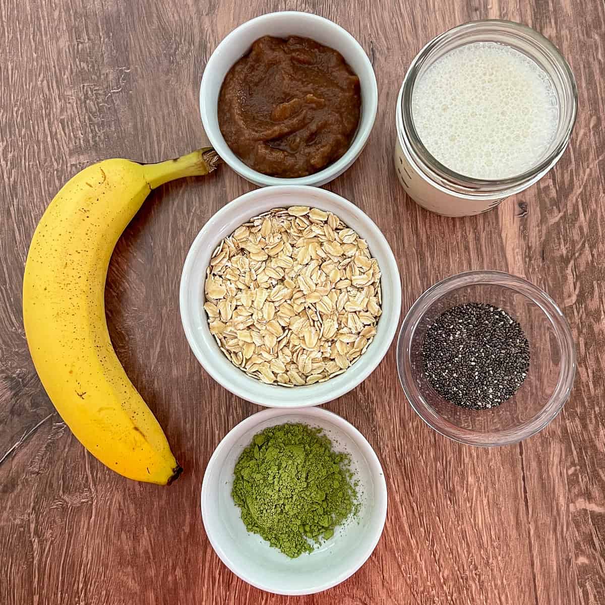 Ingredients for matcha overnight oats: rolled oats, date syrup, plant-based milk, chia seeds, matcha powder, and banana.