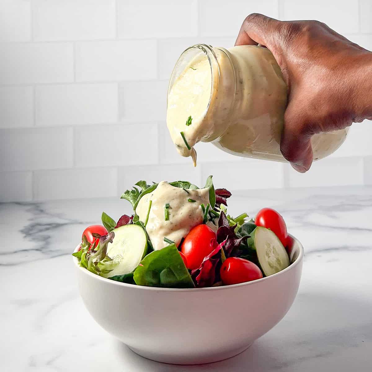 A woman's hand pouring ranch dressing over a green salad.