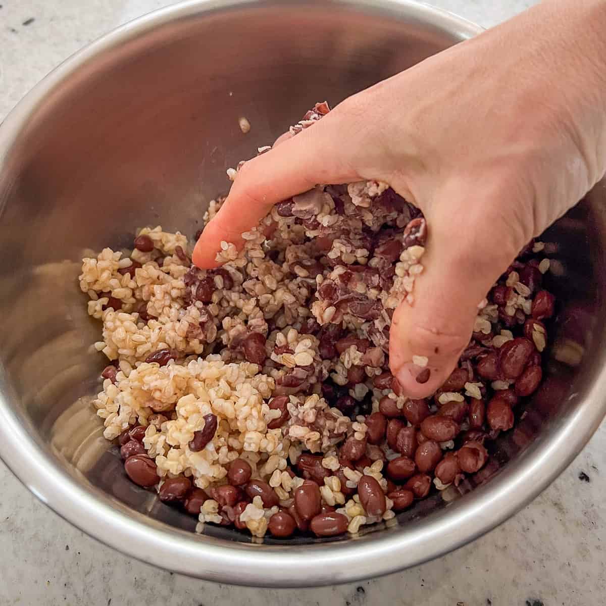 A woman's hand mashing cooked brown rice and black beans together.