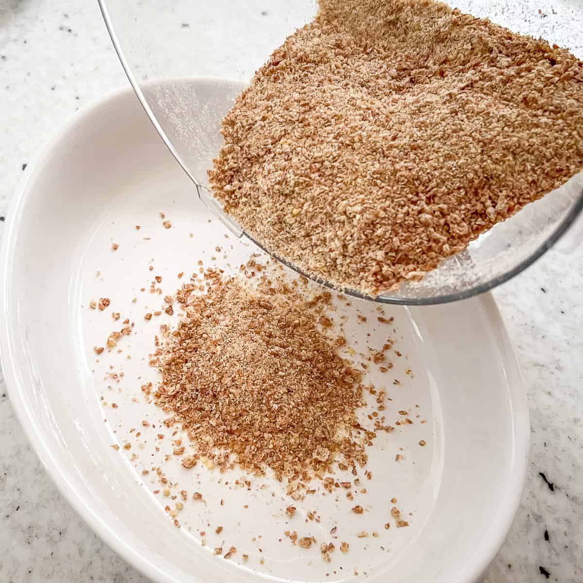 Whole grain bread crumbs being poured from the food processor into a dish.