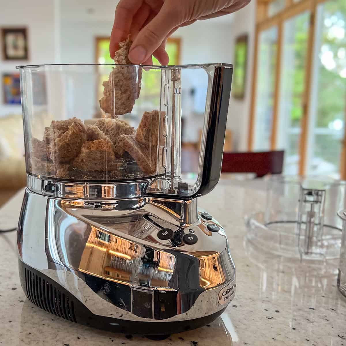 Chunks of dehydrated crisped bread being added to a food processor.