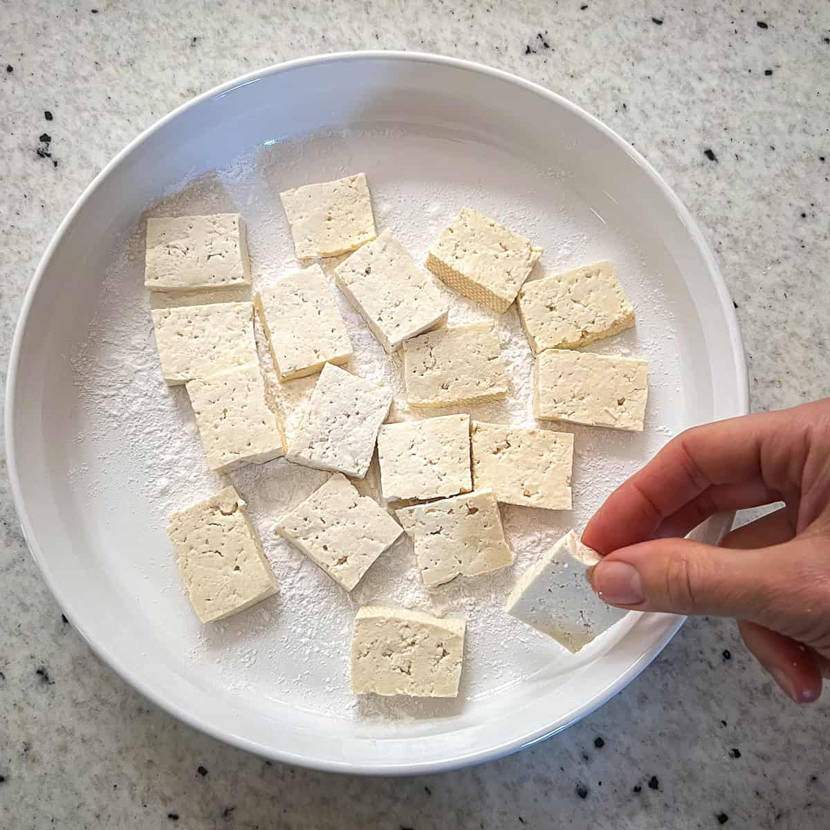 Tofu chunks being coated in arrowroot powder.