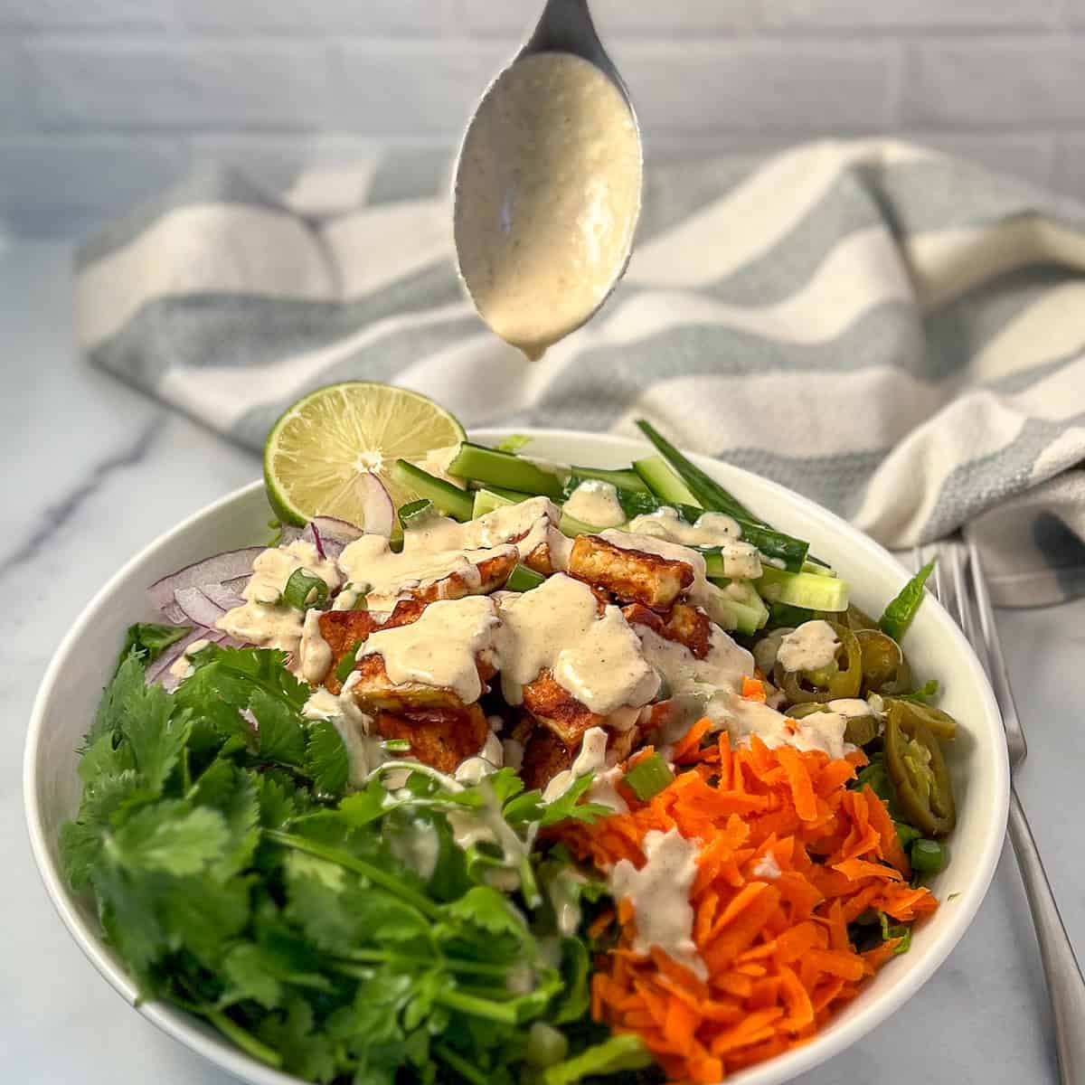 Jalapeno Lime aioli sauce being drizzled on top of vegan bahn mi salad bowl.