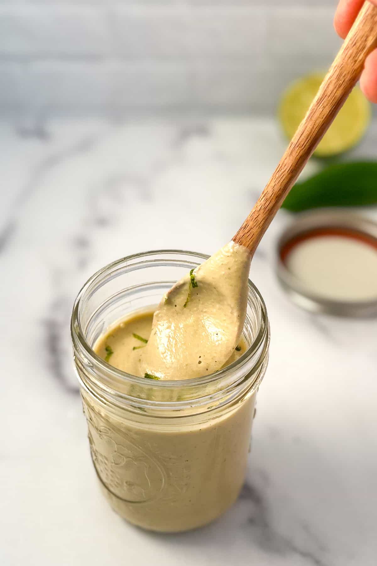 Vegan jalapeno lime aioli in a mason jar with wooden spoon to show consistency of sauce.