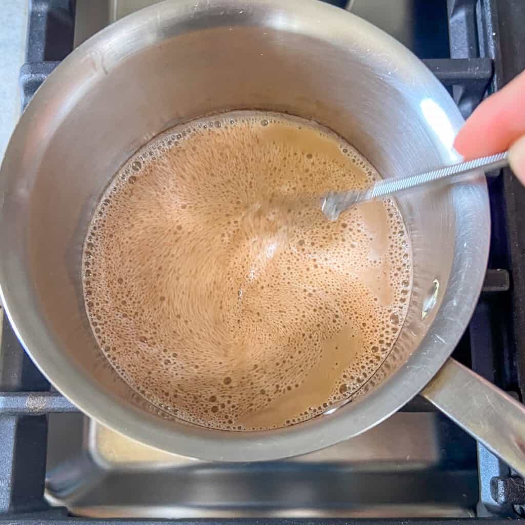 Pumpkin latte ingredients being whisked in a small pot on the stove top.