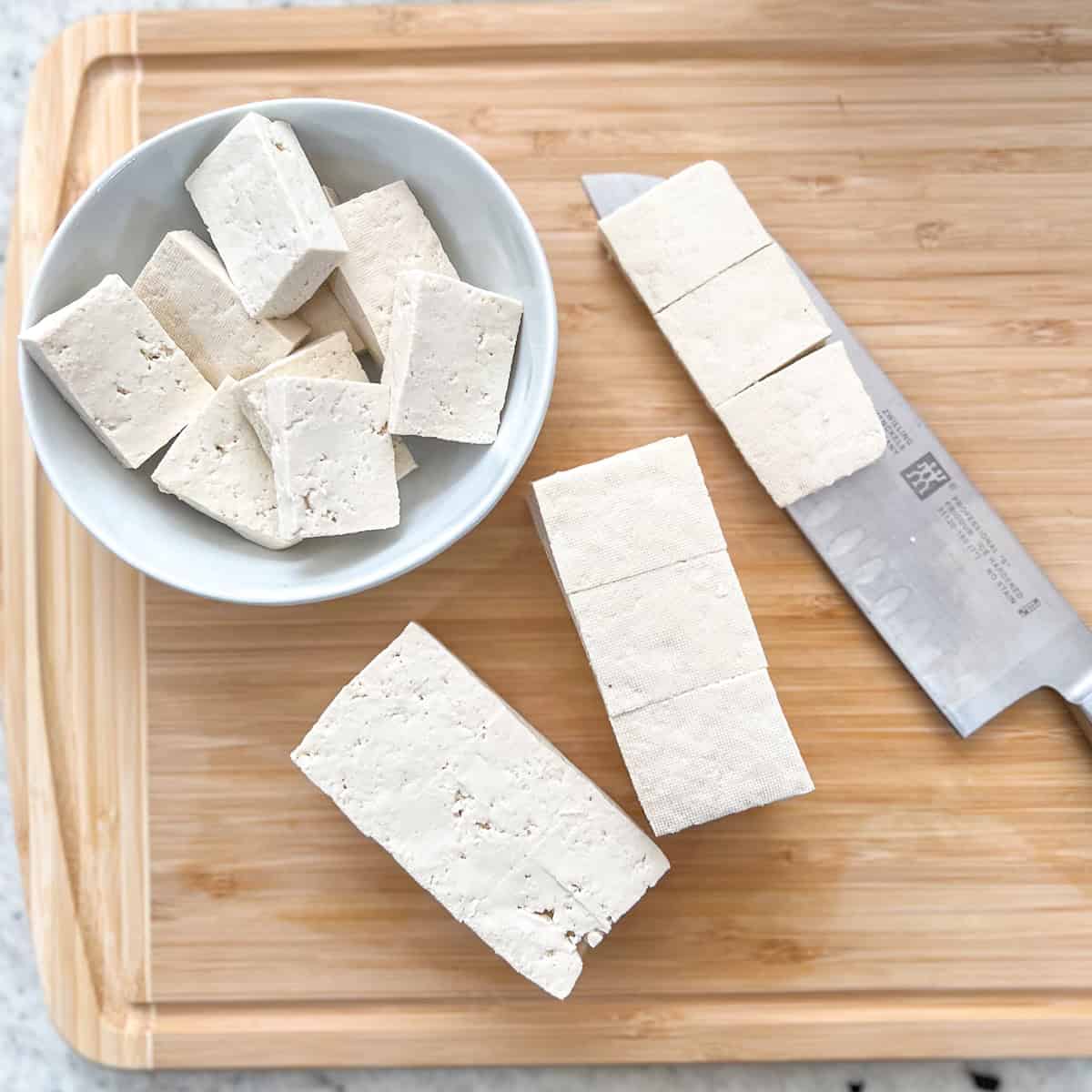 Tofu being sliced on a cutting board.