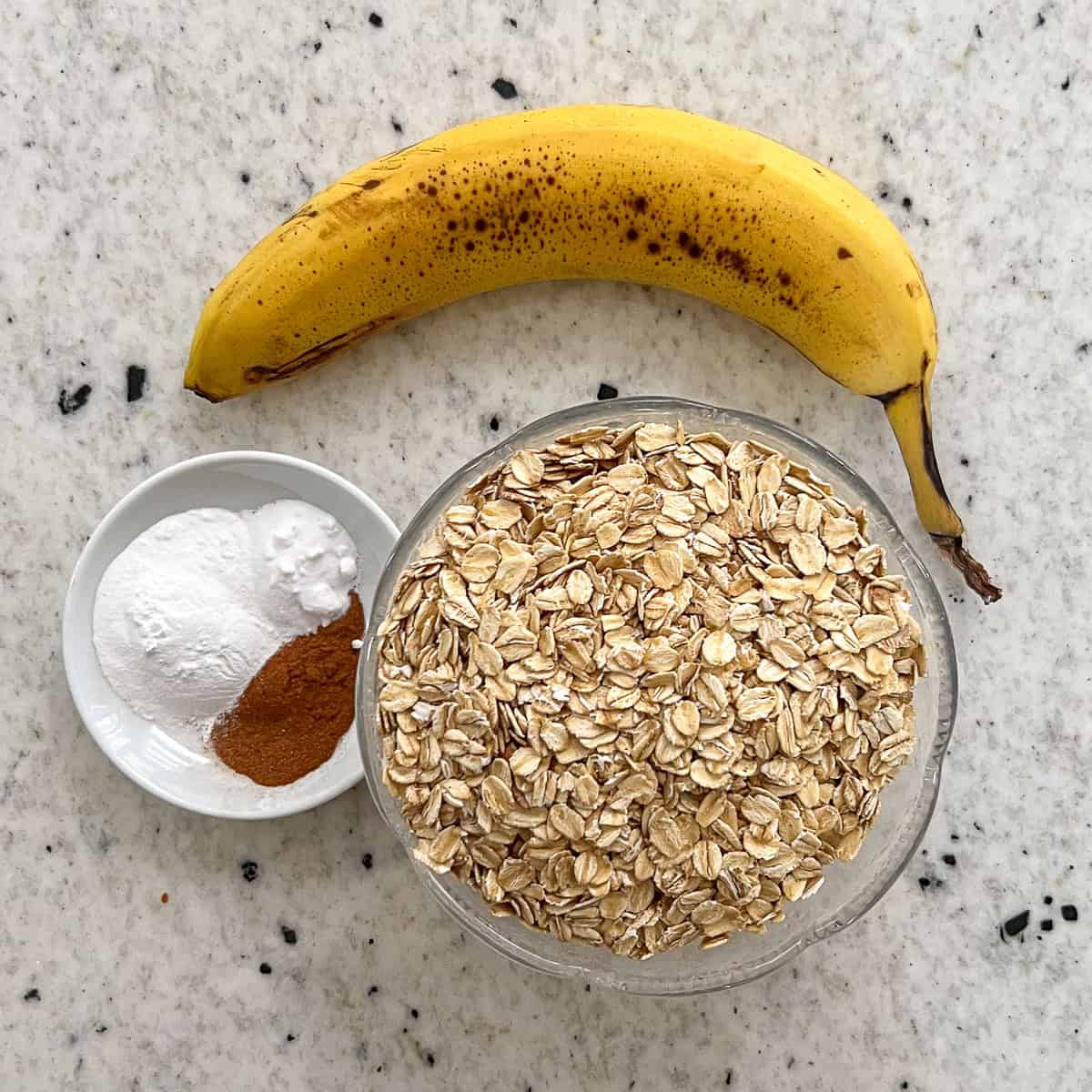 Ingredients for banana oat pancakes: Ripe banana, rolled oats, cinnamon, baking soda, and baking powder.