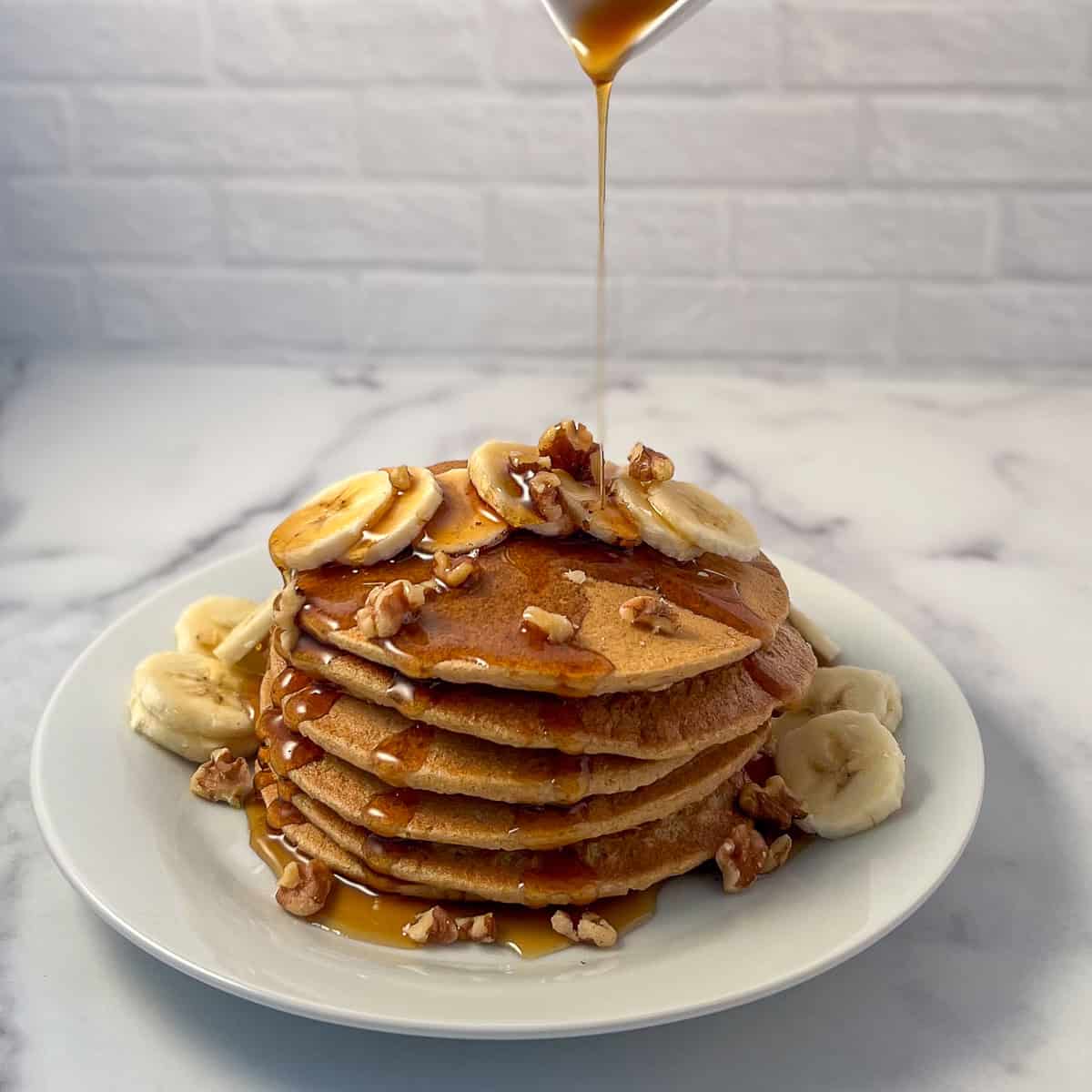 Banana oat pancakes with maple syrup being poured on top.