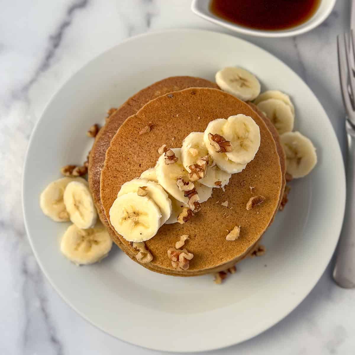 Banana oat pancakes topped with sliced banana and chopped nuts on a plate.