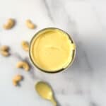 Vegan hollandaise sauce in a mason jar with loose cashews blurred in the background.