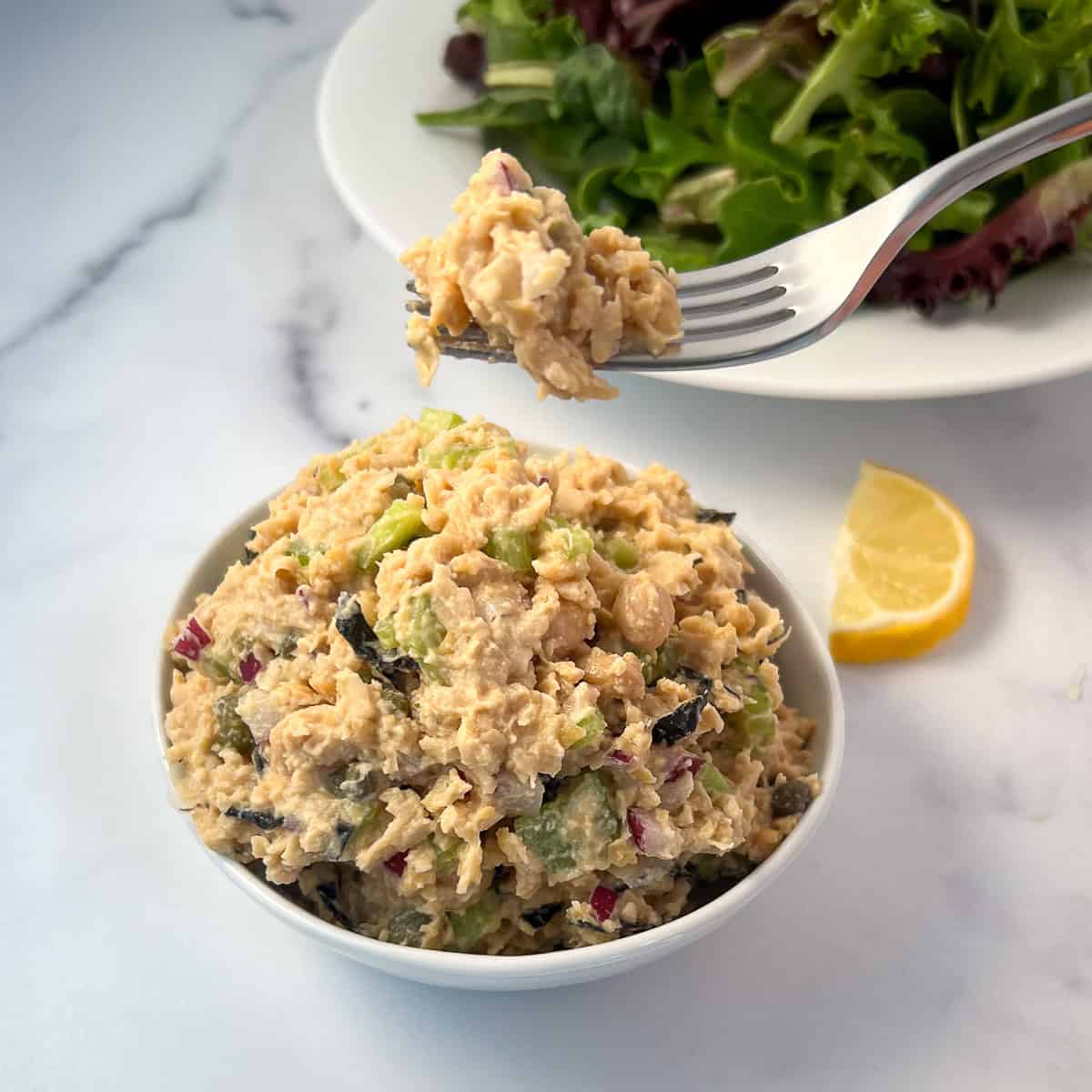 Vegan chickpea tuna salad in a bowl with a fork and salad blurred in the background.