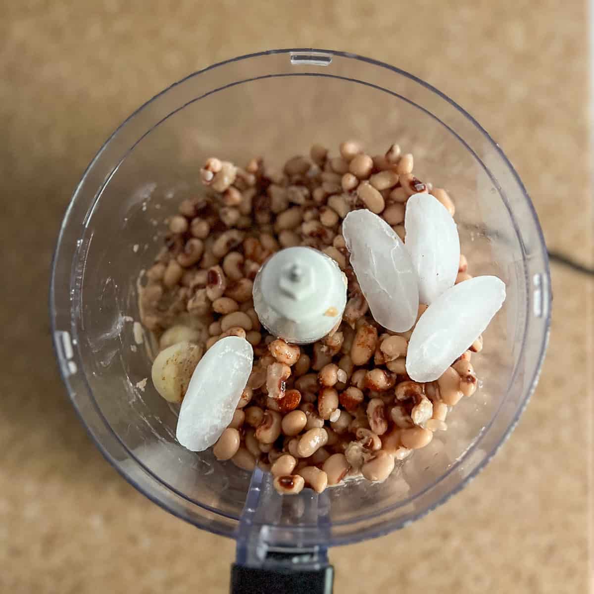 Black eyed peas, tahini, lemon juice, water, spices, garlic and ice cubes in the food processor before processing. 