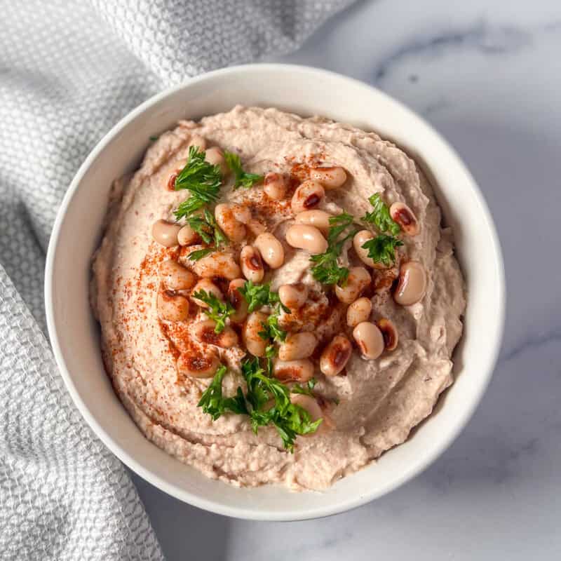 Black eyed peas hummus in a bowl with whole peas and chopped parsley.