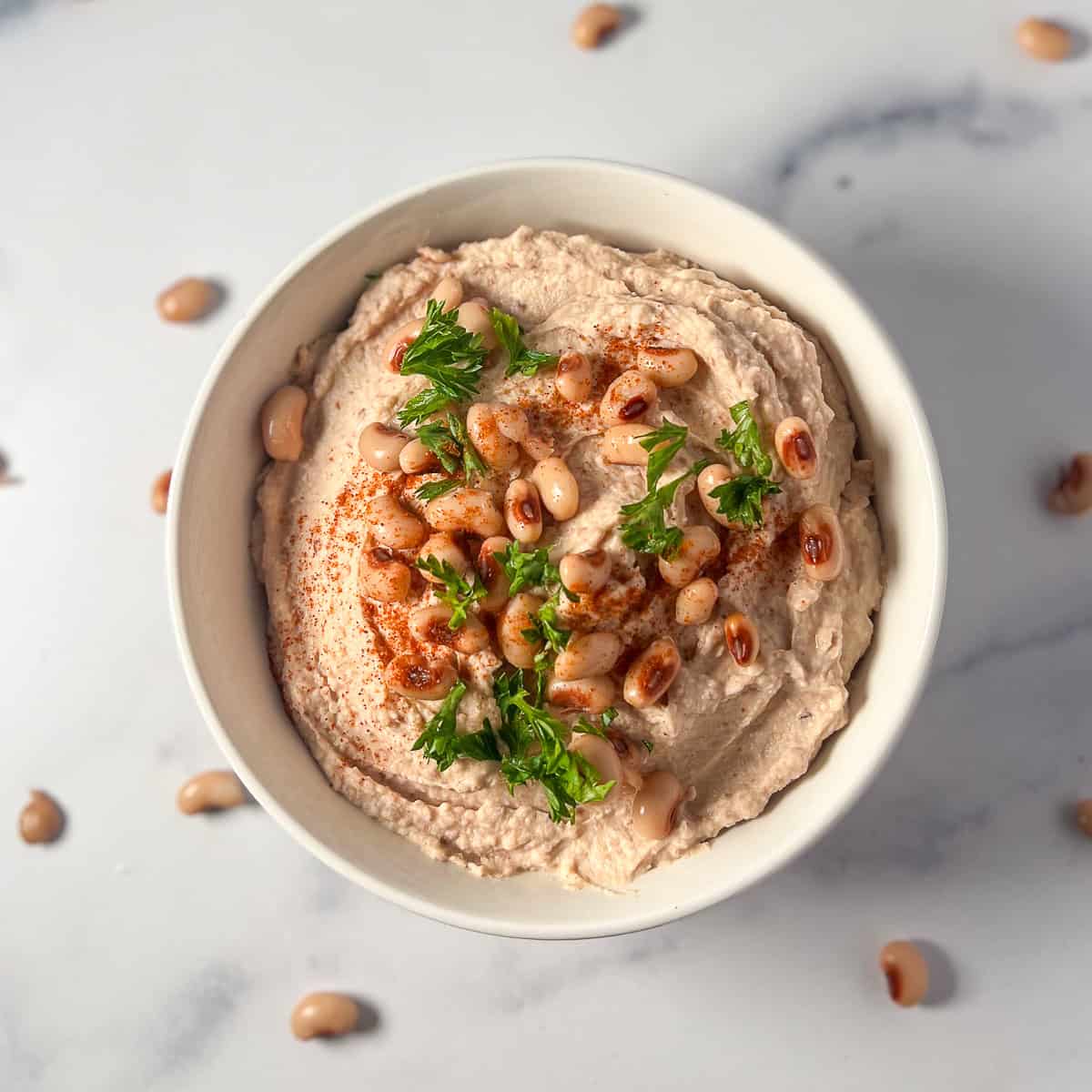 Black eyed peas hummus in a bowl topped with whole black-eyed peas and chopped fresh chopped parsley.