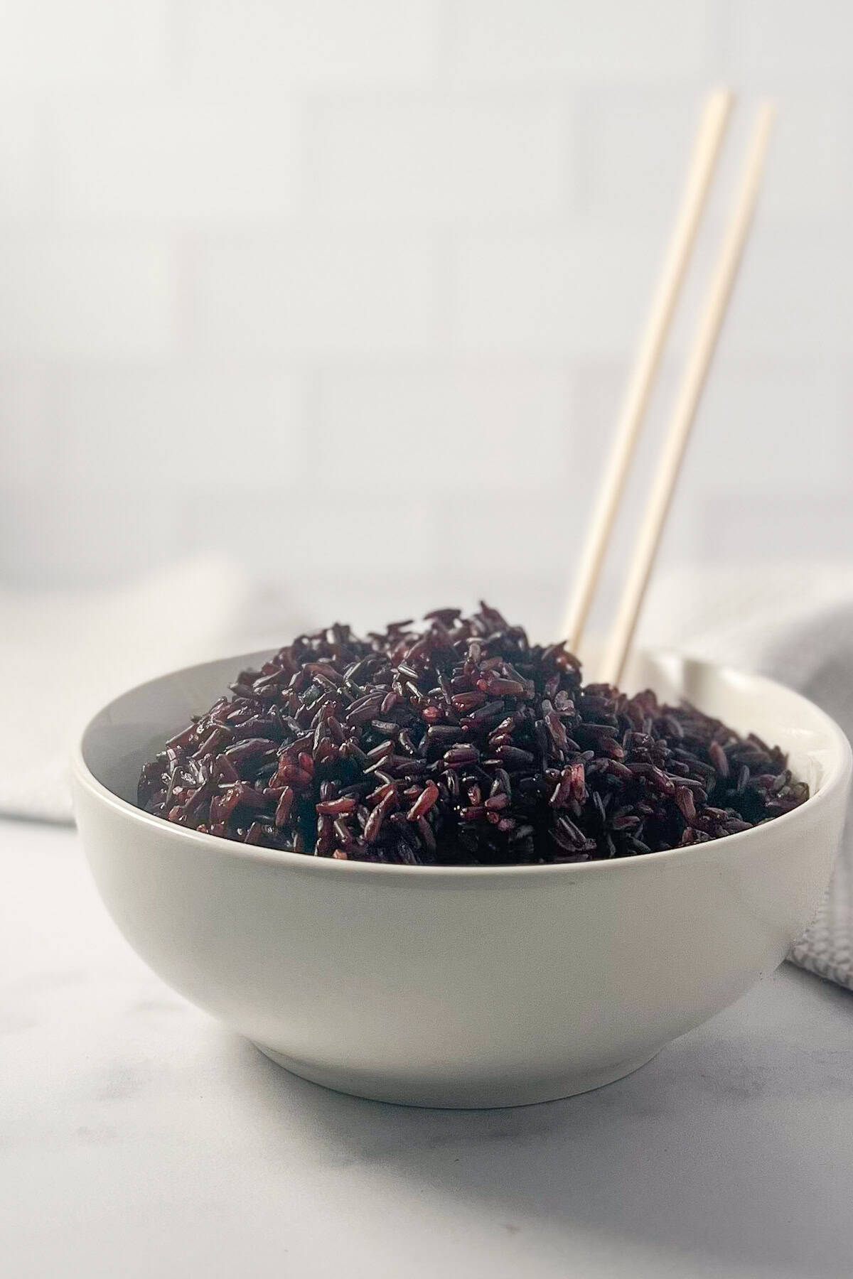 A bowl of cooked black rice with two wooden chopsticks.